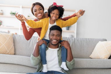 Mutlu bir aile evde, babasının omuzlarında bir çocukla eğlenirken anne sevinçle kutlama yapıyor. Sıcak atmosfer ve gülümseyen yüzler aşkı ve birliği yansıtır..