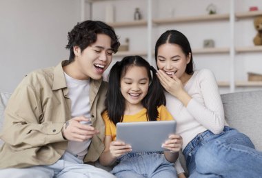 Üç aile ferdi bir kanepede oturup tabletteki bir gösterinin tadını çıkarıyorlar. Yetişkinler eğlenceyi paylaşırken ortadaki genç bir kız geniş bir gülümseme sergiliyor..