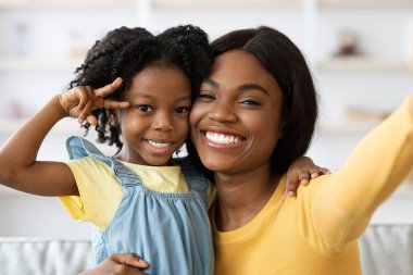 İki gülümseyen birey neşeli bir hareketle birlikte poz veriyor, gün boyunca neşeli bir yaşam alanında samimi bir sevinç ve bağlantı anı yakalıyorlar..