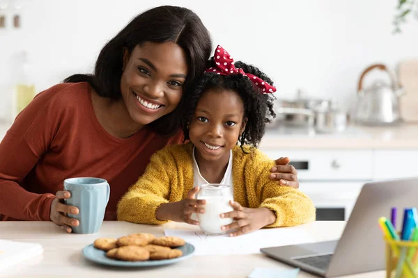 Neşeli bir anne ve kızı aydınlık bir mutfakta sıcak bir anı paylaşıyorlar. Bardaklarını tutuyorlar ve bir masanın üzerinde kurabiyelerle çevrili, bağlarını ve mutluluklarını sergiliyorlar..