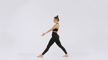 Bir kadın yoga antrenmanında, temiz, parlak bir stüdyoda esneme hareketleri yapıyor. Hareketleri onun esnekliğini ve kendini sağlıklı, aktif bir yaşam tarzına adadığını gösteriyor..