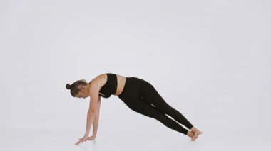 A woman is actively engaged in a yoga stretch, demonstrating strength and balance. She is dressed in a sporty outfit and appears focused in a spacious, well-lit studio promoting wellness.