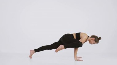 Atletik giyinen bir kadın, dayanıklılığını ve esnekliğini vurgulayan zorlu bir yoga pozu sergiler. Dekor minimalist bir stüdyo. Aktif yaşam tarzını ve fitness 'e olan bağlılığını vurguluyor..