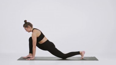 Bir kadın yoga yapar, esnekliği ve gücü vurgulayan derin bir esneme hareketi yapar. Aktif kıyafet giyer ve parlak, sakin bir stüdyoda paspasın üzerinde pratik yapar..