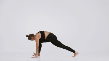 Bir kadın, hareketli bir yoga pozu vererek esnek ve güçlü bir görünüm sergiliyor. Parlak, minimalist arka plan onun hareketlerine ve sağlıklı yaşam tarzına odaklanmasını sağlar..