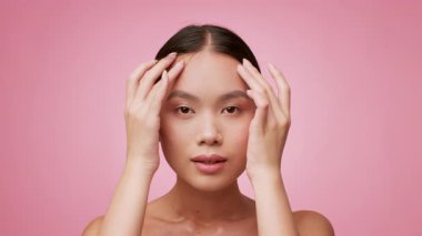 Güzel genç bir kadın şımartıcı bir cilt bakımı rutinine girer. Yüzüne nazikçe masaj yapar, parlak pembe bir arka planın önünde durup, parlak cildini gösterir..