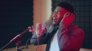 Yetenekli bir sanatçı Afrikalı Amerikalı adam, iyi donanımlı bir kayıt stüdyosunda mikrofona tutkuyla şarkı söylüyor. Enerjik atmosfer yaratıcılık sürecini güçlendirir.