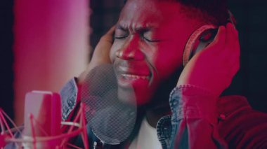 Bir şarkıcı, profesyonel ekipman ve loş ışıklandırmayla çevrili, kulaklıklarla zanaatına dalmış bir müzik stüdyosunda kayıt yaparken büyüleyici bir performans sergiliyor..