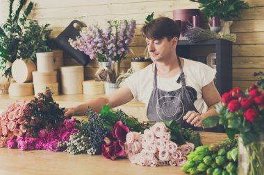 Çiçek teslimatçısı. Çiçek buketi yapan bir çiçekçi. Çiçek tasarım stüdyosunda dekorasyon ve düzenlemeler yapan bir erkek asistan ya da mal sahibi. Düzen oluşturuluyor