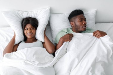 Bir çift yatakta, bir partner hayal kırıklığına uğramış ve kulaklarını tıkarken diğeri huzur içinde uyuyor..