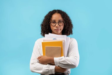 Genç siyah bir kız öğrenci kameraya şüpheyle bakarken elinde defterler ve kağıtlar tutuyor. Üniversite deneyimini mavi stüdyo geçmişiyle karşılaştırıyor..