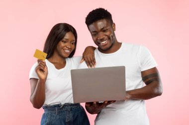 A joyful African American couple is engaged in online shopping using a laptop.