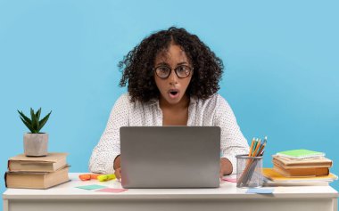 Genç siyahi kadın, dizüstü bilgisayarında gördüklerinden ürkmüş bir şekilde masada oturuyor. Etrafı kitaplarla ve kırtasiyelerle çevrili olarak, mavi bir arkaplan üzerinde çalışıyor, bir proje hatasının farkına varıyor..