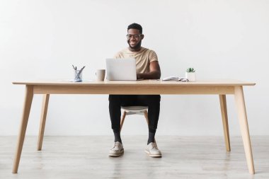 Genç siyah adam evindeki bir masada oturuyor ve bir dizüstü bilgisayar üzerinde çalışıyor. Uzaktan kumandalı işiyle meşgul gibi görünüyor, rahat ortamın tadını çıkarıyor..