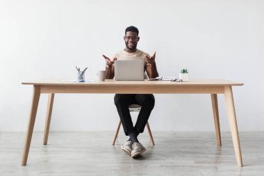 Yakışıklı, bin yıllık siyahi bir adam evindeki bir masada oturuyor ve bir video görüşmesi yapıyor. Rahat bir çalışma alanından iletişim kurarken dizüstü bilgisayar ve jestler kullanıyor..