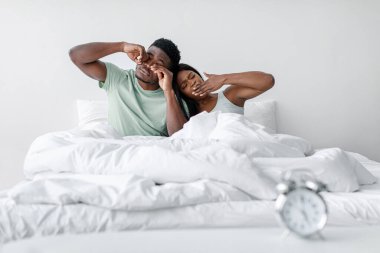 Bir çift yatakta oturur, gözlerini ovuşturur ve uyandıktan sonra esnerler. Oda aydınlık, beyaz yatak ve sabahın erken saatlerini gösteren bir saat var..