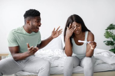 Parlak bir yatak odasında, bir çift yatakta oturur, görünür bir şekilde güçlü duygular ifade ederler. Kadın hamilelik testi yaparken, erkek heyecanlı görünüyor..