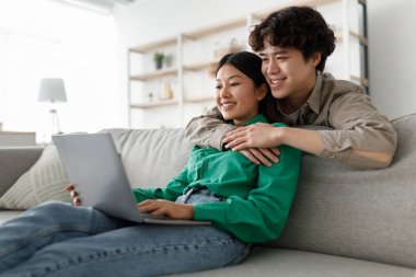 Sevgi dolu çift kanepelerinde oturup dizüstü bilgisayar kullanırken birbirlerine sarılıyorlar. İnternette mutlu mesut geziniyorlar ve rahat evlerinde birbirlerine eşlik ederek eğleniyorlar..