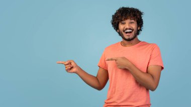 Yakışıklı bir doğu milenyumu adamı mavi bir stüdyo geçmişine karşı duruyor, açık alanı işaret ederken heyecan gösteriyor. Sıradan giyinmiş ve heyecan verici bir teklifi paylaşmaya hazır görünüyor..