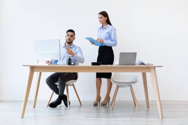 Kendine güvenen erkek patron, çağdaş bir ofiste genç bir kadın stajyere yeni bir projeyi açıklıyor. Modern bir masada dizüstü bilgisayarlarla oturmuş detayları tartışıyorlar..