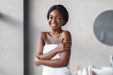 Genç siyah bir bayan beyaz bir havluya sarılmışken kameraya gülümsüyor. Etrafı şık bir banyoyla çevrili ferahlatıcı bir sabah duşundan sonra teninin ipeksi dokunuşlarını sever..