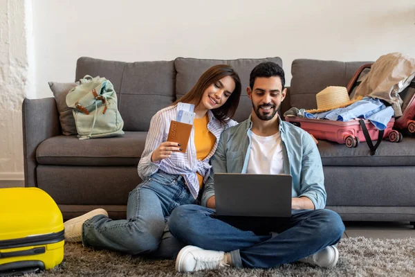 İki kişi yerde oturuyor, etrafı bavullarla çevrili. Kadın uçuş biletlerini tutarken ve ortağına gülümserken mutlu bir şekilde seyahatlerini planlıyorlar..