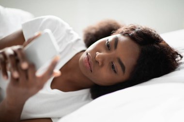 Kıllı saçlı genç bir Afro-Amerikalı kadın yatakta uzanıyor, akıllı telefonuna odaklanıyor. Mesajlaşırken üzgün görünüyor. İlişkilerinde zorluklar ve endişe hisleri var..