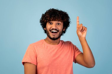 Pembe tişörtlü neşeli bir Hindu adam mavi bir stüdyoda duruyor. Geniş bir şekilde gülümsüyor ve işaret parmağını havaya kaldırıyor. Son zamanlarda ortaya çıkan bir fikir için heyecanlanıyor..