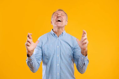 Olgun bir adam sarı turuncu bir stüdyoda parmaklarını çapraz yapıp gözlerini kapatıyor. Dilek tutarken umut verici bir ifade sergiliyor. Beklenti ve inancı somutlaştırıyor..