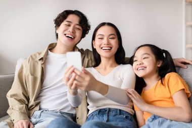 Üç arkadaş kanepede oturup birlikte selfie çekerken kahkahalarını paylaşıyorlar. Keyifli atmosfer, rahat bir ortamda rahatlarken bağlantılarını ve eğlenceli ruhlarını vurgular..