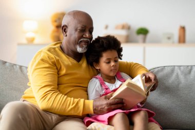 Yaşlı bir adam ve genç bir kız bir oturma odasında bir kanepede oturup bir peri masalı kitabına odaklandılar. Kız kıvırcık saçlı ve büyükbabasının okuduğu hikayeleri dinlerken konsantre olmuş görünüyor..