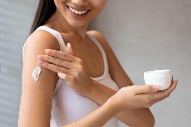 Beyaz bluzlu esmer kadın omzuna tereyağı sürüyor, sabah duşundan sonra mutlu bir şekilde gülümsüyor. Elinde bir krema kavanozu var, kendine baktığı anın altını çiziyor..