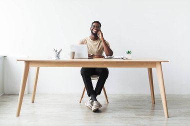 Siyah bir işadamı, masasında otururken, bir dizüstü bilgisayar ve notlarla çevrili bir telefon görüşmesinden zevk alır. Aynı gülüşü paylaşıyor. Parlak bir stüdyo ortamında olumlu bir konuşma atmosferi olduğunu gösteriyor..