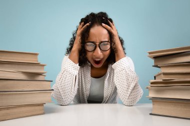 Genç bir Afro-Amerikalı kız öğrenci etrafı sayısız kitapla çevrili, gözle görülür şekilde sıkıntılı bir şekilde oturuyor. O, başını tutarken hayal kırıklığı içinde çığlık atar, sıkı çalışmaktan bitkinliğini ifade eder..