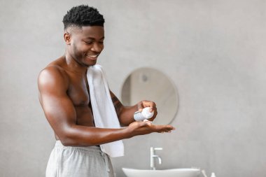 İyi giyimli Afro-Amerikan bir adam şık bir banyoda duruyor ve eline tıraş köpüğü sürüyor..