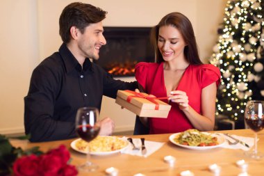Bir erkek, samimi bir akşam yemeği sırasında bir kadına güzel bir hediye sunar. Etrafları şenlikli süslemelerle çevrili ve yemeklerini birlikte yiyorlar..