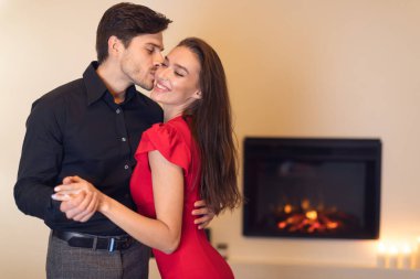 Bir çift, yumuşak ışıklı bir odada dans ederken hassas bir anın tadını çıkarıyor. Şöminenin sıcaklığı, gülümsemeleri ve yakınlıklarını paylaştıkça romantik ortamı daha da güzelleştiriyor..