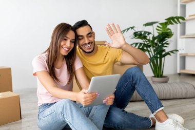 Yeni oturma odalarının zemininde oturmuş tablet üzerindeki bir video görüşmesinin keyfini çıkarırken birkaç gülümseme. Etrafları hareket eden kutular ve bitkilerle çevrili, canlı bir atmosfer yaratıyorlar..