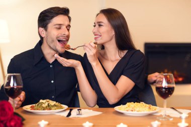 Bir çift yemek boyunca sevgi dolu bir anın tadını çıkarıyor. Yumuşak ışıklandırma ve güllerle dolu bir masada makarna ve şarap paylaşıyorlar. Sıcak bir atmosfer yaratıyorlar..