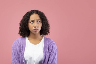 Genç siyahi bir kadın pembe bir stüdyo ortamında düşünceli bakışlarını kaçırıyor. Üzgün ya da kuşkulu görünüyor, kendi düşüncelerinde kaybolmuş. Yüzündeki ifade derin düşünce ve endişeyi yansıtıyor..