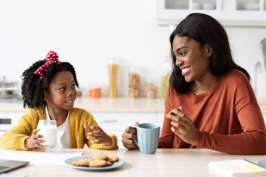 Bir anne ve kızı modern bir mutfakta eğlenceli ve sıcak bir anı paylaşıyorlar. İçkinin ve kurabiyelerin tadını çıkarırken gülümsüyorlar. Birlikte güzel anılar yaratıyorlar..