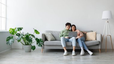 Sevgi dolu bir Asyalı çift rahat bir koltukta oturup birlikte film izlerken dizüstü bilgisayarlarını paylaşıyorlar. Mutlu ve meşguller, sıcak bir evde online eğlencenin tadını çıkarıyorlar..