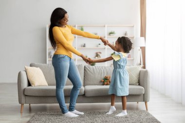 Bir anne ve küçük kızı davet edilen oturma odalarında neşeli bir dans ediyorlar. Yumuşak güneş ışığı büyük pencerelerden süzülür kahkahaları ve gülümsemeleri paylaşırken.