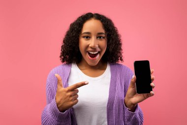 Hevesli siyah bir kadın akıllı telefonuna boş bir ekranla işaret ediyor, canlı pembe bir arka plan karşısında yeni bir uygulama veya web sitesi sergiliyor. Bu sahne mobil reklamcılığın özünü yakalar..