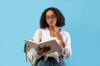 Düşünceli bir Afrikalı Amerikalı bayan öğrenci ev ödevini düşünürken bir kitap okuyor. Bir kalem tutuyor, gözlük takıyor, ve mavi bir stüdyonun arka planında duruyor, düşüncelere dalmış..