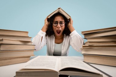 Öfkeli genç siyah bir kadın kitaplarla çevrili bir masada oturuyor. O, hayal kırıklığı içinde bağırırken başına bir kitap koyuyor. Arka plan mavi, çalışmaktan duyduğu üzüntüyü yansıtıyor..