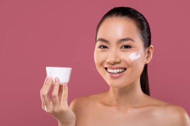 Asyalı güzel bir bayan elinde yaşlanma önleyici krem kavanozuyla gülümsüyor..