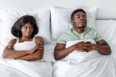 Yatak odasında, bir erkek huzur içinde uyurken yanındaki kadın hayal kırıklığına uğramış gibi görünür. Vücut dilleri gerginlik gösteriyor, konuşulmamış sorunları ortaya çıkarıyor. Ayarlar samimi ama çelişkili görünüyor.