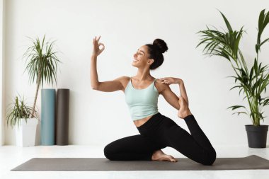 Parlak bir yoga stüdyosunda, genç bir esmer kadın denizkızı pozu veriyor, neşeli bir ifade ve iyi bir jest sergiliyor. Esnek birey egzersiz yaparken mutluluk yayar..