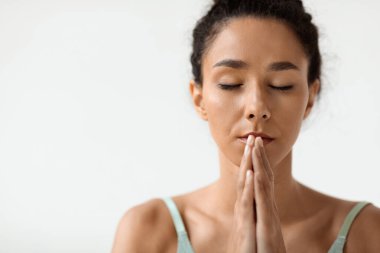 Sakin esmer bir kadın, sakin bir ortamda meditasyon yapıyor. Yüzünün yanında iç huzuru ve farkındalığı teşvik eden namaste bir jest yapıyor..